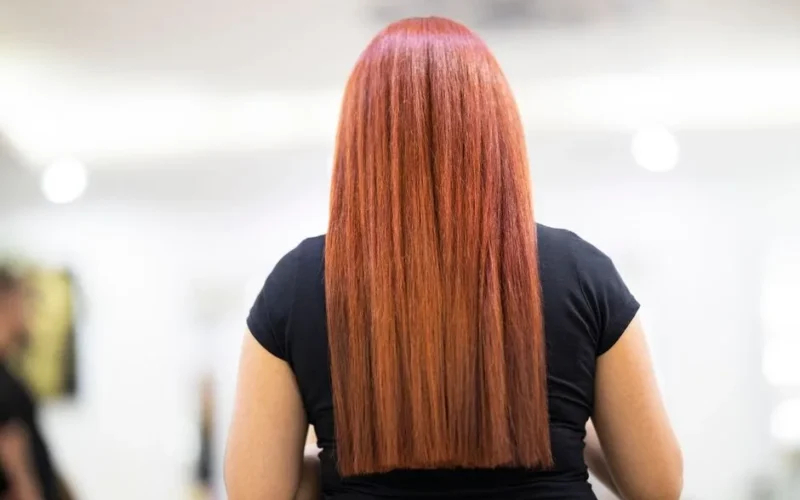 A woman with straight, vibrant red hair seen from the back, showcasing a fresh hairstyle in a professional salon.