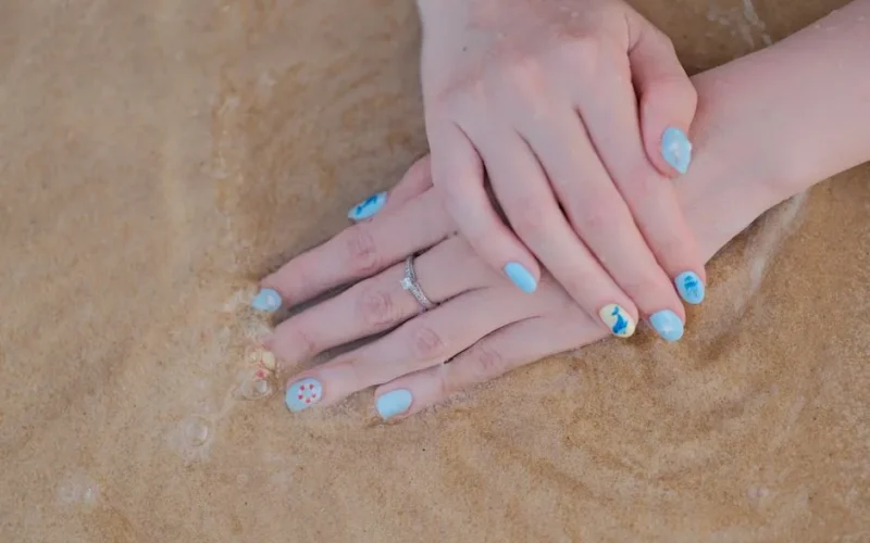 A serene close-up of hands with beach-themed nail art against sandy beach waves.