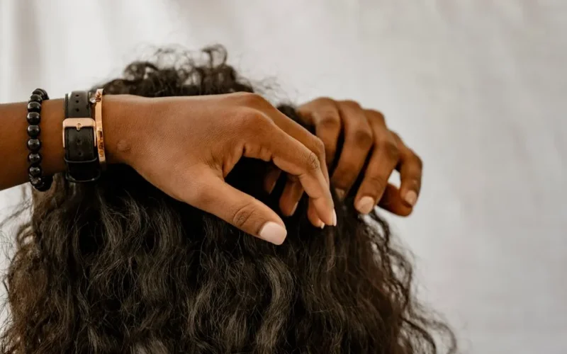 Detailed image of hands styling curly hair, showcasing accessories and a natural hairstyle.