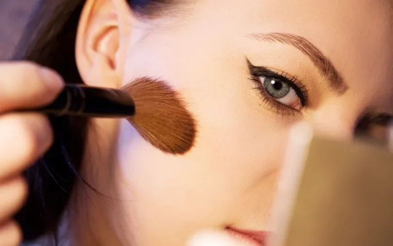 A close-up shot of a woman applying makeup with a brush.