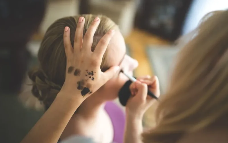 Close-up of a makeup artist applying cosmetics to a woman's face indoors.