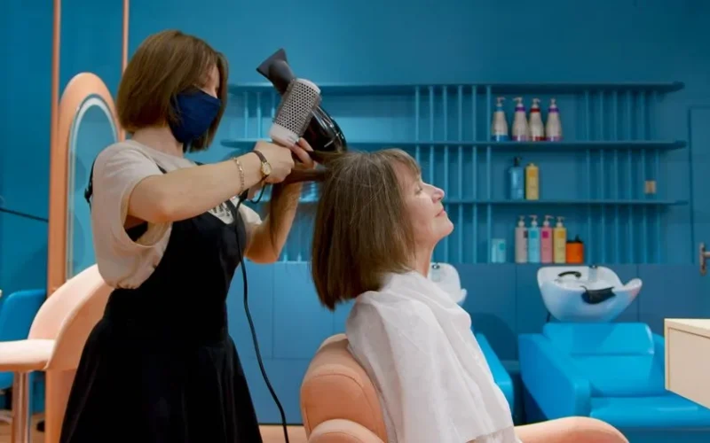 Hairdresser styling senior woman's hair with blow dryer in chic salon setting.