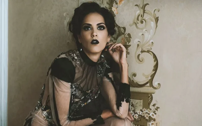 Sophisticated portrait of a woman with bold black lipstick, styled in glamour fashion, set against an ornate wallpaper.
