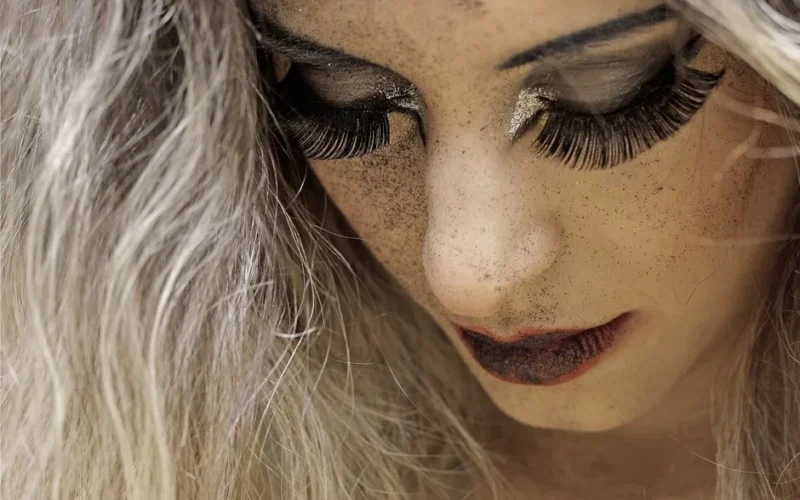 Close-up portrait of a woman with dramatic eye makeup and long eyelashes, highlighting her artistic look.