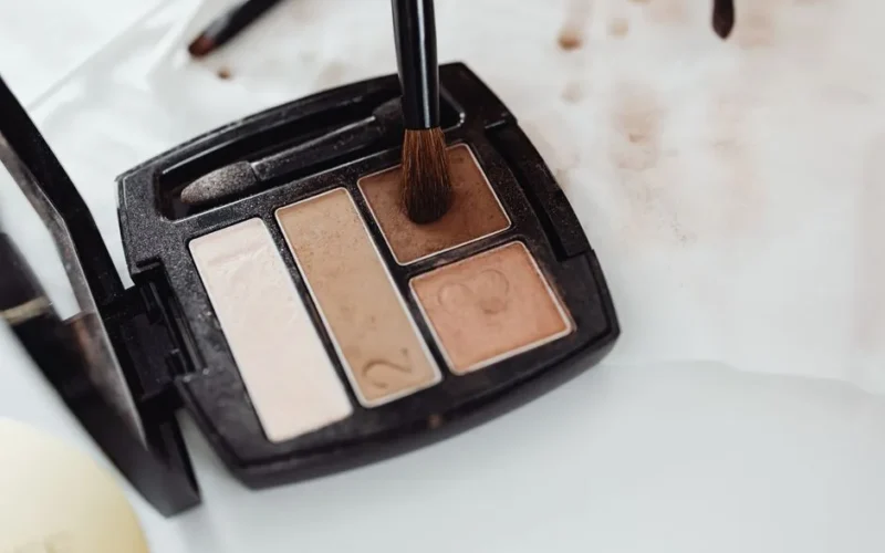 Close-up of a makeup eyeshadow palette in neutral shades with a brush touching the product surface.