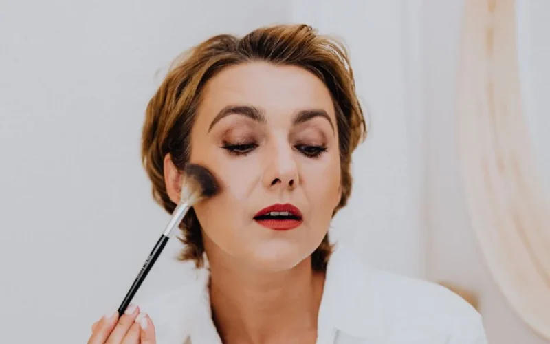 Close-up of an adult woman enhancing her beauty with makeup using a brush, exuding elegance and glamour.