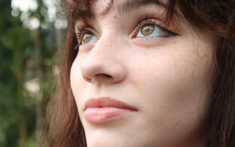 A close-up portrait capturing the natural beauty of a woman with brown hair and freckles, gazing upwards.