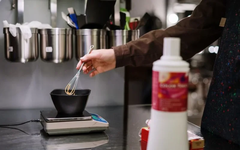 A stylist prepares hair dye with precision using professional tools in a salon setting.