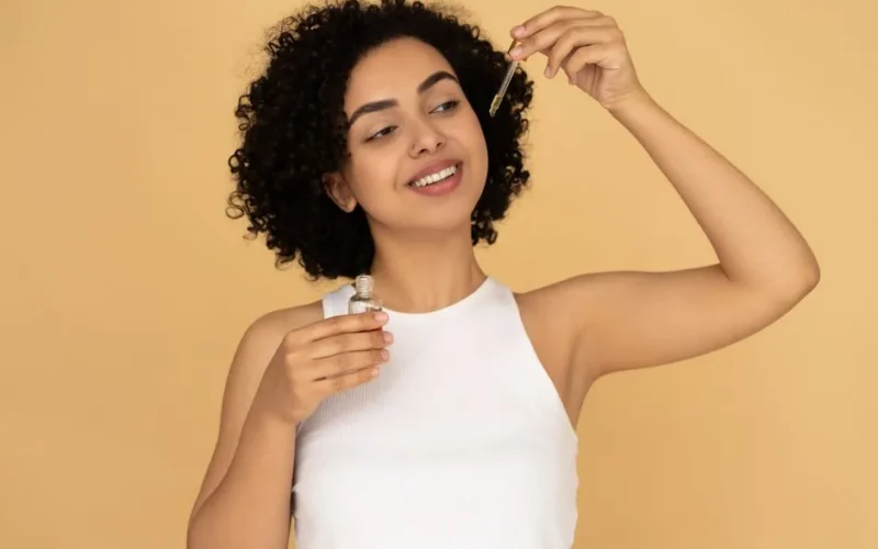 A smiling woman with curly hair applying essential oil for healthy skin care.