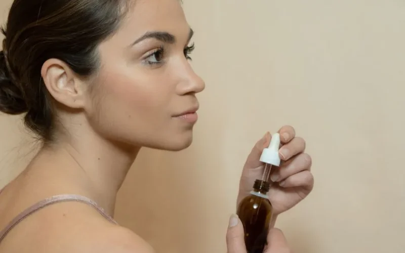 Side profile of a young woman holding a dropper bottle for skincare routine.