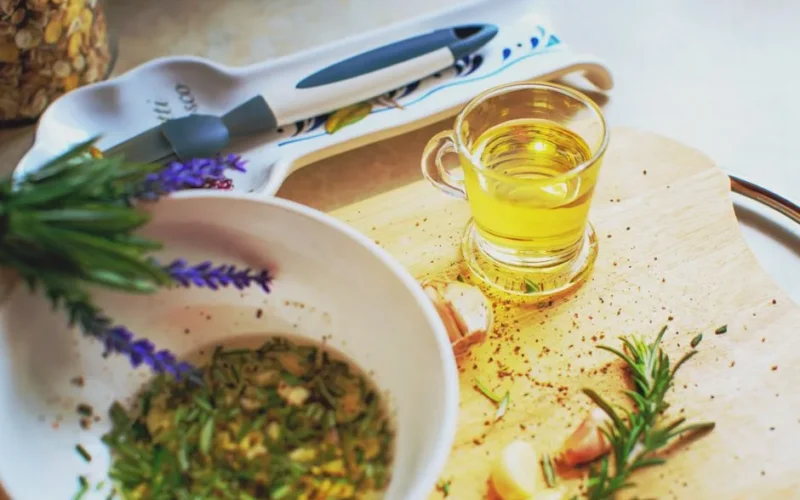 Close-up of herb-infused oil preparation with rosemary and garlic on a wooden board.