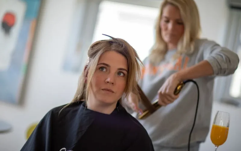 Woman in salon cape receiving professional hair styling indoors by hairdresser.