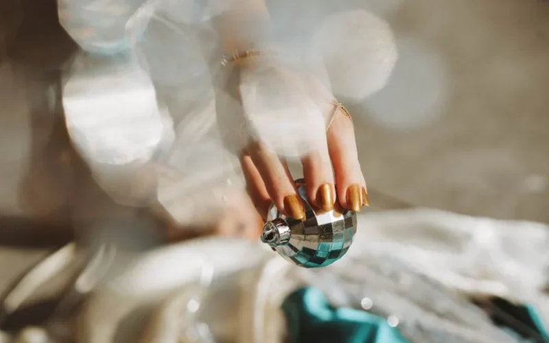 A close-up of a hand with manicured nails holding a shiny Christmas bauble, capturing holiday elegance.