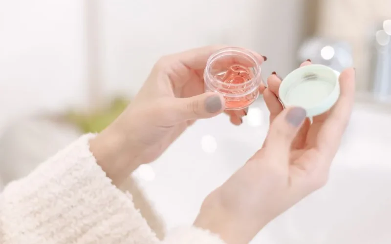 Close-up of a woman applying moisturizer from a container, showcasing soft hands and gentle care.