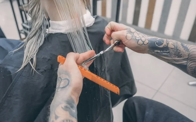 Close-up of a stylist's tattooed hands cutting wet hair in a modern beauty salon.