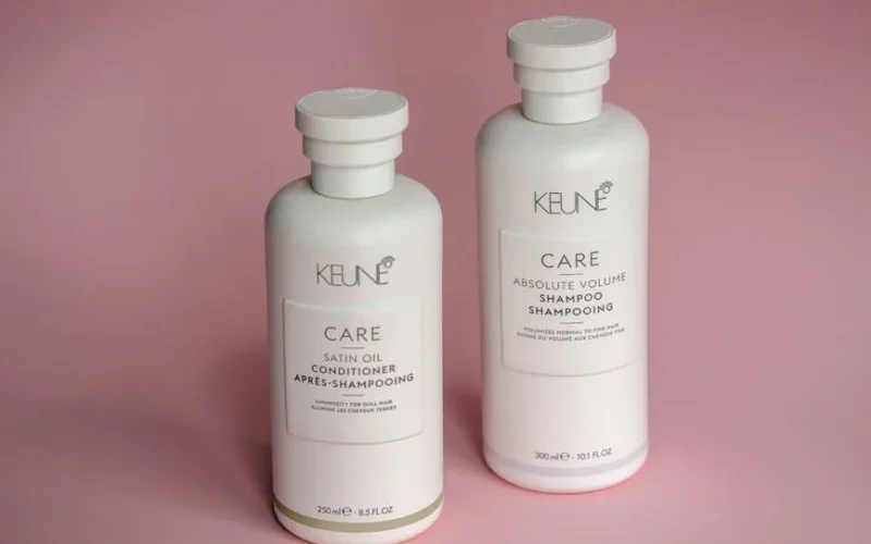 White Keune shampoo and conditioner bottles on a soft pink background.