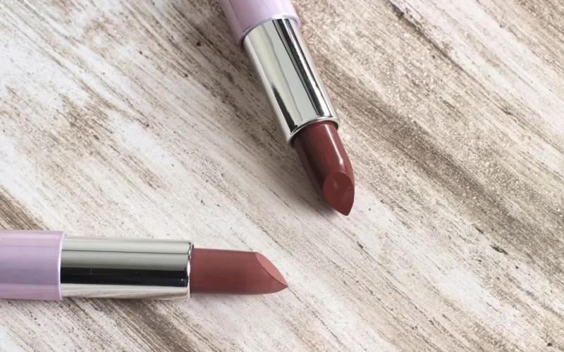 Close-up of two elegant lipsticks on a rustic wooden surface, showcasing beauty and style.