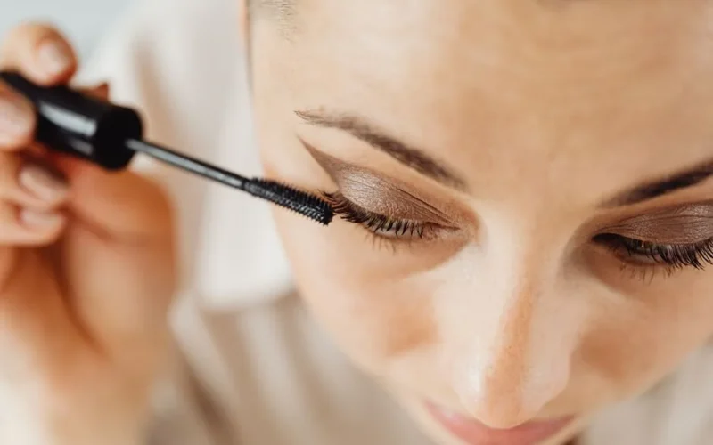 A woman applying mascara to her eyelashes enhances her beauty in a detailed close-up shot.