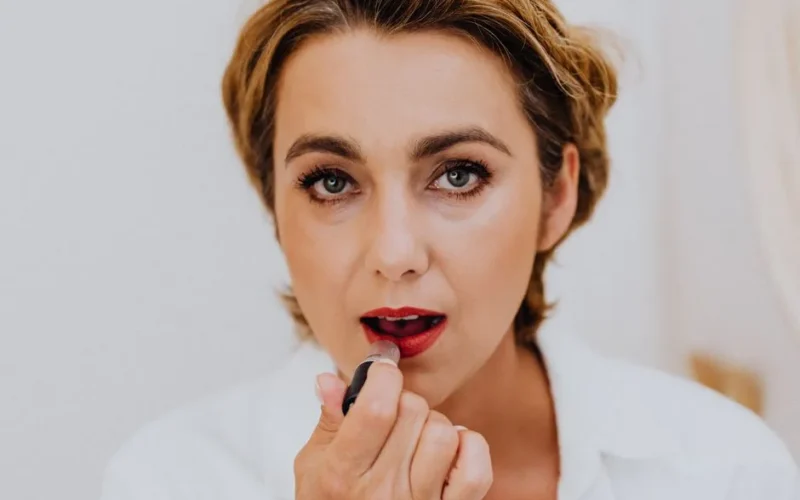 Close-up of an adult woman applying red lipstick, showcasing beauty and elegance