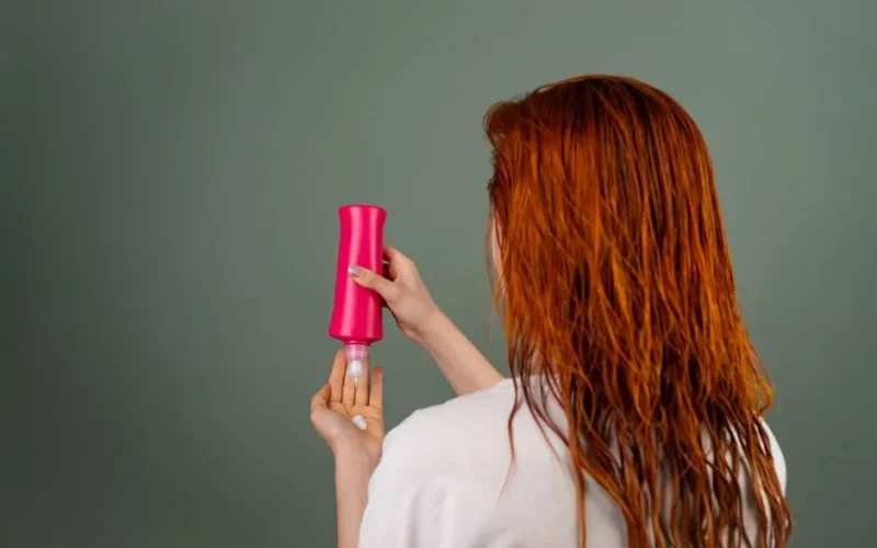 Adult woman with wet red hair applying conditioner. Hair care routine.