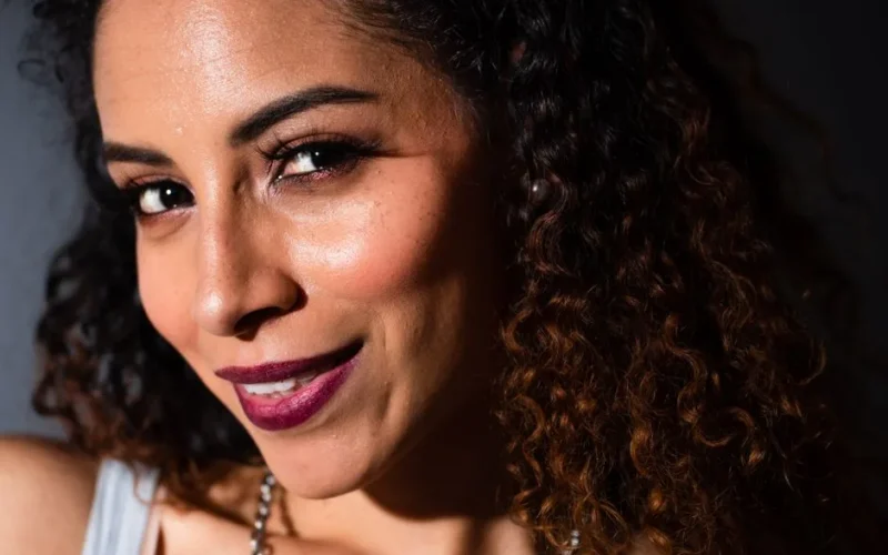 Close-up portrait of a smiling woman with curly hair and makeup, exuding elegance and confidence.
